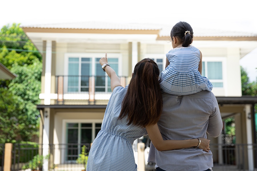 Personal Insurance - Portrait of a Happy Family, Father, Mother and Daughter Standing in Front of New Home on a Bright Sunny Day with Backs Turned Toward Camera
